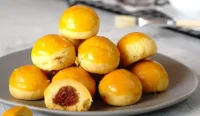 Toples berisi kue nastar bulatan kuning mengilap berisi selai nanas khas Lebaran Indonesia yang berasal dari adaptasi kue tart Belanda
